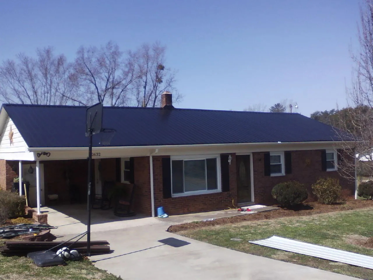 Finished dark blue metal roof on a brick ranch with a carport in Howard