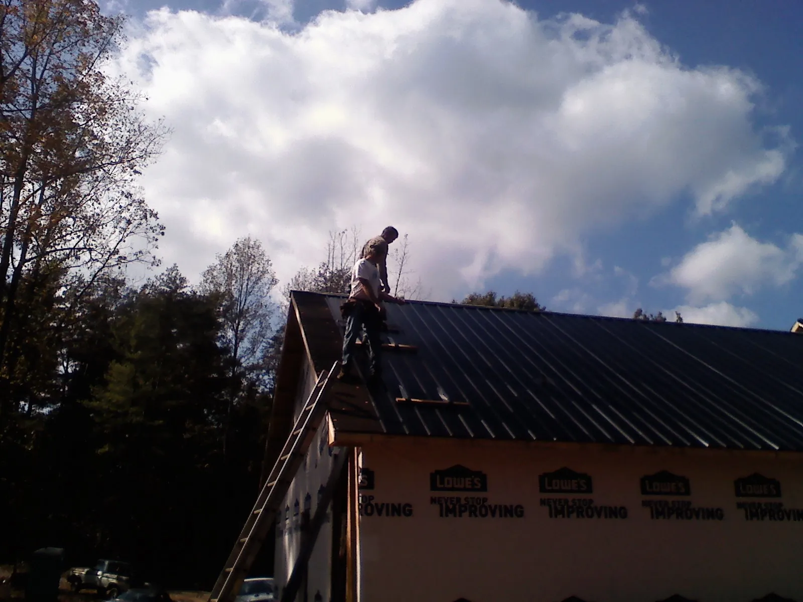 Roofer fastening dark metal panels high against a cloudy sky, from a Roof Inspection job in Howard